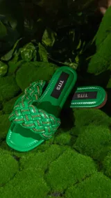 Sandalias bajas color verde con tiras trenzadas y detalles de cadena dorada.