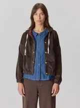 Campera de corte holgado con textura aterciopelada y estampado de cuadros sutil. Presenta cuello con cordones ajustables, cierre frontal con botones y mangas largas con puños elásticos.