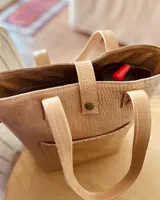 Bolso matero color beige con textura croco, con correa larga regulable y bolsillo exterior para lentes.