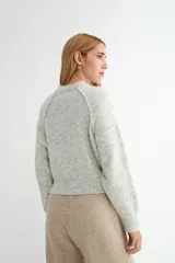 Buzo de tejido de punto con cuello redondo, diseño cropped y mangas largas con puños acanalados. Presenta una textura jaspeada en tono beige.
