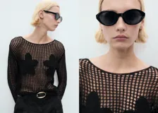 Jersey de punto grueso negro con cuello barco, manga larga y detalles florales bordados en el frente.