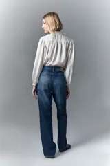 Jean de corte recto y tiro alto confeccionado en denim azul rígido. Presenta un diseño de hotfix brillante aplicado sobre la superficie del pantalón. Cuenta con cierre y botón frontal.