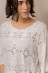 Blusa de punto calado color blanco, con diseño geométrico y floral transparente, escote redondo y mangas tres cuartos amplias de calce relajado.