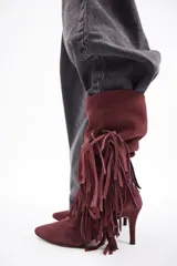 Bota de caña alta confeccionada en cuero vacuno color bordó, con diseño de flecos laterales y taco fino.