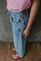 Pantalón de jean tiro medio con diseño barrel, caracterizado por su pernera holgada que se estrecha hacia el tobillo. Presenta cinco bolsillos, cierre frontal con cremallera y botón, y detalle de raya planchada en el frente.