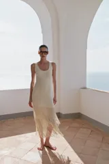 Vestido midi de escote redondo y sin mangas, confeccionado en tejido con textura. Presenta un diseño recto con bajo acabado en capas de flecos largos al tono.