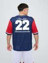 Remera de fútbol Umbro del Club Nacional de Football, de diseño tricolor con cuerpo azul marino, mangas y canesú rojos, y cuello en V con detalles en blanco y azul. Incluye el logo de Umbro en el pecho derecho y el escudo del club en el izquierdo.