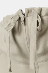 Sudadera tipo bomber de tejido suave, color beige, con cuello alto ajustable mediante cordones, cierre frontal con cremallera, mangas largas con puños elásticos y bolsillos laterales de vivo.