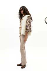 Chaleco reversible de gamulán de oveja en color natural, con corte holgado, cuello a la base y terminaciones al corte. Presenta tiras de cuero en el frente para atar.