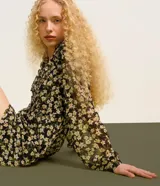 Vestido corto de chiffon negro con estampado de flores blancas y amarillas, escote en V, mangas largas abullonadas y volados en el busto.