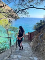 Vestido largo tejido de algodón color negro, sin mangas, con cuello redondo y tajos laterales. Presenta dos bolsillos de cuero color marrón en el frente.