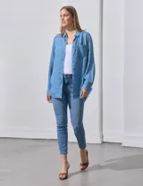 Camisa celeste de tencel, marca Hester & Orchand. Tiene cuello con solapa, escote en V, abertura central con botones, bolsillo aplicado en el frente y ruedo desflecado.