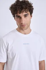 Remera blanca de algodón, corte holgado, con cuello redondo y un pequeño logo bordado en azul claro en el pecho.
