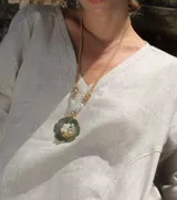 Collar con dije dorado en forma de flor con incrustaciones de perlas, con tiras de cuero sintético color beige que se atan al cuello.
