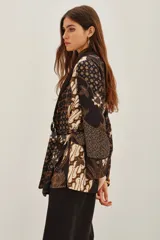 Saco tipo kimono con estampado batik en tonos marrones y negros, con solapas lisas, mangas largas y lazo ajustable en la cintura. Incluye bolsillos frontales y forro interior.