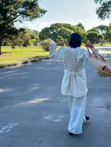 Camisa larga tipo sobrecamisa o abrigo ligero, color verde menta pálido con estampado floral en tono amarillo claro. Presenta escote en V con atado frontal mediante lazos, mangas largas con detalle fruncido y puños con flecos en tono turquesa.