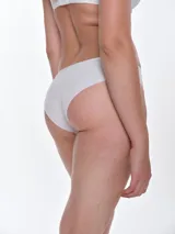 Bombacha tipo bikini confeccionada en tul con detalles de encaje floral. Presenta un pequeño lazo decorativo en el centro de la cintura y un diseño de cobertura media.