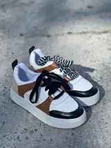 Zapatillas urbanas de cuero sintético color blanco, con puntera y talón en negro, laterales en marrón y cordones negros.