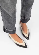 Chatita de cuero bicolor, punta fina, con diseño en forma de V en el empeine. La punta y el borde inferior son negros, mientras que el resto del cuerpo es color crema (off-white).