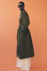 Trench oversize de Zara Woman Collection, color verde militar, con cuello solapa, cierre frontal cruzado con botones y cinturón ajustable del mismo tejido. Presenta mangas largas con trabillas ajustables y bolsillos delanteros.