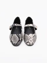 Ballerina de estilo Mary Jane con estampado de piel de serpiente en tonos grises y negros. Cuenta con una tira ajustable sobre el empeine con hebilla metálica dorada y suela plana.