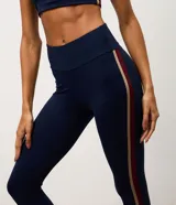 Legging deportiva de tiro alto en color azul marino, con franjas laterales en contraste de color bordó y beige. Confeccionada en microfibra elástica, ofrece un ajuste ceñido y cómodo para actividades físicas.