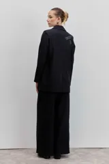 Blazer negro de rayas finas blancas, con solapas, cierre de botón frontal y broches decorativos en la solapa.