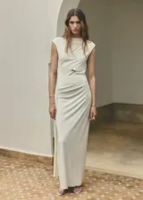 Vestido largo recto color crudo, con cuello redondo, manga corta, detalle drapeado en la cintura y espalda abierta.