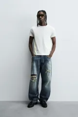 Camiseta de corte relajado, color gris claro, confeccionada en tejido con estructura waffle. Presenta cuello redondo y manga corta, con costuras decorativas en contraste color dorado que recorren los laterales y los hombros.