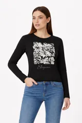 Remera de manga larga color negro, con cuello redondo a la base. Presenta un estampado frontal cuadrado con diseño floral en tonos blanco y negro, acompañado por la palabra 'Elegance' en tipografía cursiva con efecto foil.