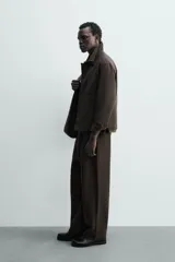 Pantalón de corte relajado con pliegues frontales, bolsillos laterales y bolsillos traseros de vivo. Presenta cierre frontal con cremallera y botón.