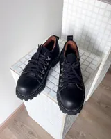 Zapatos tipo borceguíes bajos de cuero vacuno negro, con cordones y ganchos metálicos. Presentan suela track dentada y costuras visibles en el borde de la suela.