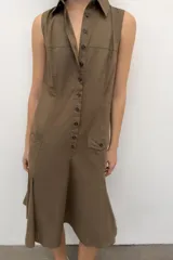 Vestido midi camisero color marrón, sin mangas, con cuello solapa y cierre frontal con botones. Presenta bolsillos delanteros con solapa y falda con pliegues en el bajo.