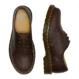 Zapato de tres ojales Dr. Martens modelo 1461, confeccionado en cuero Crazy Horse color marrón con acabado encerado. Presenta costuras amarillas características en el borde de la suela y suela de goma con cámara de aire.