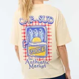 Remera de corte oversize color amarillo claro, con estampa gráfica en la espalda que representa una lata de sardinas con limón sobre un fondo de cuadrillé rojo.