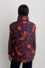 Chaleco puffer con cuello alto y cierre frontal oculto, estampado con diseño floral y de aves en tonos rojos sobre base azul oscuro.