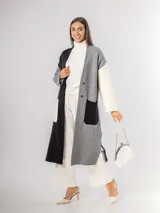 Sacón tipo tapado de corte largo, confeccionado en tejido de punto con diseño color block en tonos gris, negro y blanco. Presenta cierre frontal con botones, bolsillos laterales de parche y aberturas en los costados.
