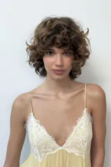 Vestido corto amarillo con escote en pico y tirantes finos ajustables. Presenta detalles de encaje blanco en el escote y en los laterales de la falda. Tiene forro interior y cierre en la espalda con cremallera y botones forrados.