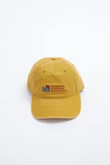 Gorra de gabardina color mostaza con visera curva y bordado frontal con texto "Uniform Outdoor Collection" y un pequeño paisaje.