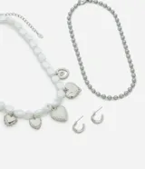 Conjunto de bijouterie de metal plateado, compuesto por dos collares y un par de aros. Incluye una cadena de esferas, un collar de cuentas orgánicas blancas estilo perla con dijes colgantes de corazones y aros, y aros pequeños tipo argolla con cierre de perno.
