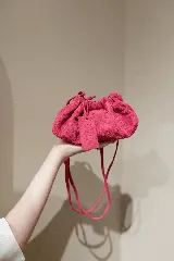 Cartera tipo sobre de cuero color fucsia, con diseño fruncido y cierre de cordón. Incluye una correa ajustable y extraíble para usarla como cartera o como sobre de fiesta.