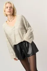 Pullover de mujer tejido en punto waffle, color beige claro con sutil tramado grisáceo. Presenta escote en V con terminación deshilachada y puños anchos en color beige liso.