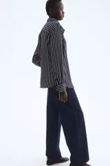 Camisa de manga larga con cuello clásico y cierre frontal de botones. Presenta un estampado de rayas verticales finas blancas sobre fondo azul marino. Los puños son anchos y también tienen rayas horizontales.