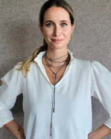 Collar estilo corbatín confeccionado en tiento de cuero color suela, con detalle de cuentas metálicas plateadas distribuidas a lo largo de las tiras.