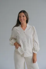 Blusa de color beige con cuello mao y cierre frontal de botones. Presenta mangas largas abullonadas con puños ajustados y un diseño con bordados en relieve de patrones orgánicos en toda la prenda.