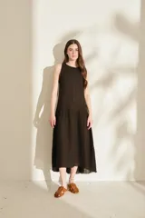 Vestido midi negro sin mangas, con cuello redondo, corte recto en la parte superior y falda amplia con vuelo. Presenta costuras decorativas verticales y un detalle deshilachado en el dobladillo inferior.