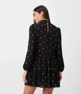 Vestido corto negro de chiffon con estampado de pequeños corazones naranjas, cuello alto, mangas largas abullonadas y falda con volados en capas.