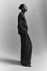 Pantalón sastrero gris oscuro de corte holgado con tiro alto, cierre con corchete y botón ocultos. Presenta piernas amplias con pinzas, raya marcada en el frente y la parte trasera, bolsillos al bies y bolsillos decorativos en la parte posterior.