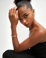 Pulsera rígida dorada de aleación de metales bañada en oro 18k, con dos cristales facetados multicolor en forma triangular en los extremos.