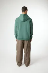 Hoodie de color verde musgo con efecto lavado, corte holgado, capucha con cordones y bolsillo canguro frontal. Presenta un pequeño logo en forma de 'X' en el pecho.